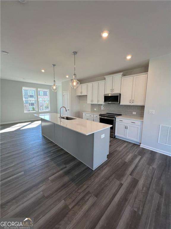 kitchen with pendant lighting, sink, white cabinetry, stainless steel appliances, and an island with sink