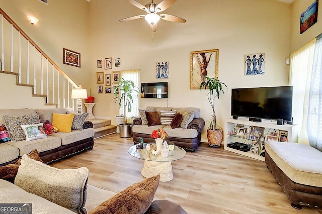 living room with a towering ceiling, ceiling fan, and light hardwood / wood-style flooring