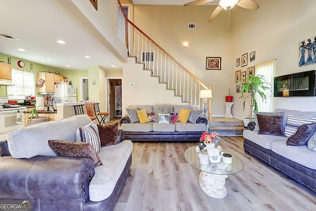 living room featuring ceiling fan, light hardwood / wood-style flooring, and a high ceiling