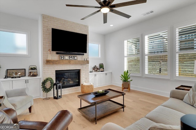 living room with a brick fireplace, ceiling fan, and light hardwood / wood-style flooring