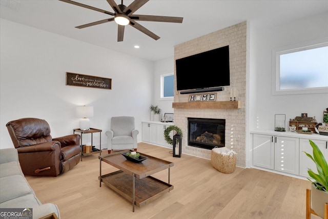 living room with a brick fireplace, light hardwood / wood-style flooring, and ceiling fan