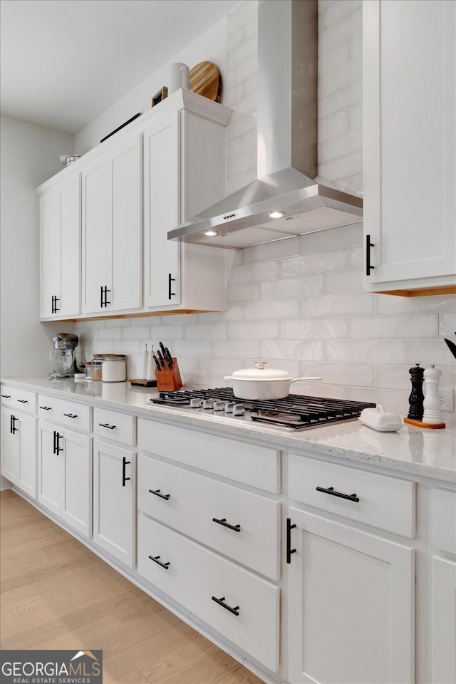 kitchen featuring white cabinets, backsplash, and wall chimney exhaust hood