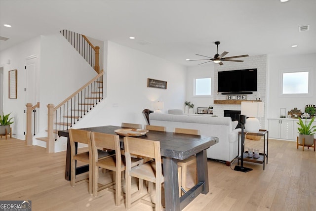 dining space featuring ceiling fan, a large fireplace, and light wood-type flooring