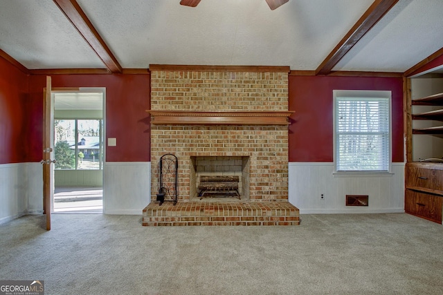 unfurnished living room featuring a brick fireplace, a textured ceiling, carpet flooring, ceiling fan, and beam ceiling