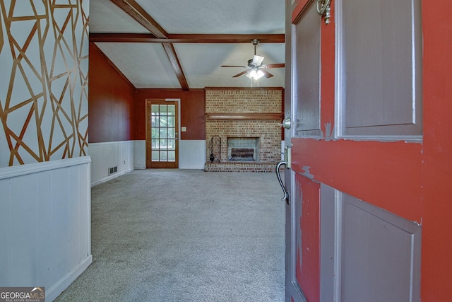 unfurnished living room featuring carpet floors, ceiling fan, vaulted ceiling with beams, and a fireplace