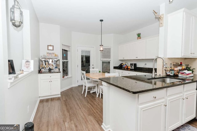 kitchen with sink, dark stone countertops, white cabinets, decorative light fixtures, and light wood-type flooring