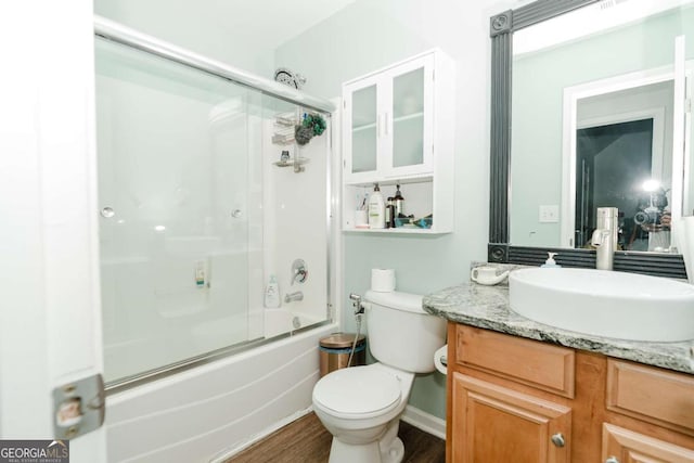 full bathroom with vanity, hardwood / wood-style flooring, bath / shower combo with glass door, and toilet