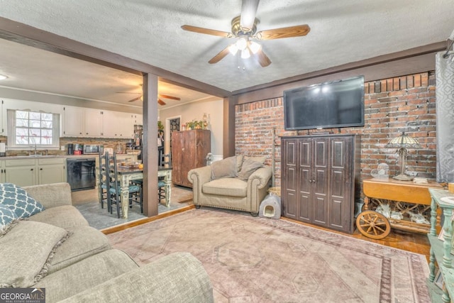 living room with ceiling fan, sink, a textured ceiling, and brick wall