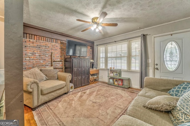 living room featuring brick wall, hardwood / wood-style floors, ornamental molding, ceiling fan, and a textured ceiling