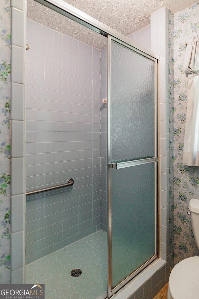 bathroom with a textured ceiling, a shower with shower door, and toilet