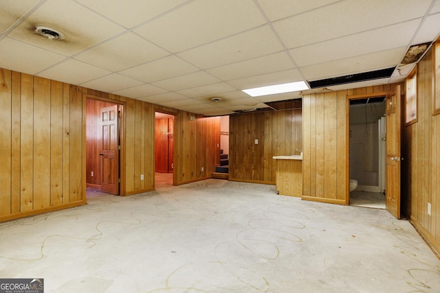 basement featuring a drop ceiling and wooden walls