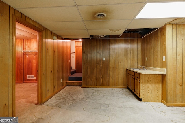 bathroom with vanity, wooden walls, concrete flooring, and a drop ceiling