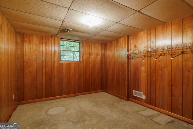 basement with a paneled ceiling, light colored carpet, and wood walls