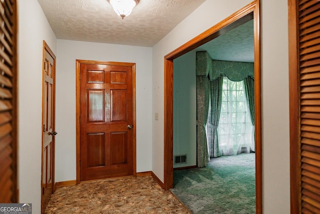 hallway with a textured ceiling and carpet flooring