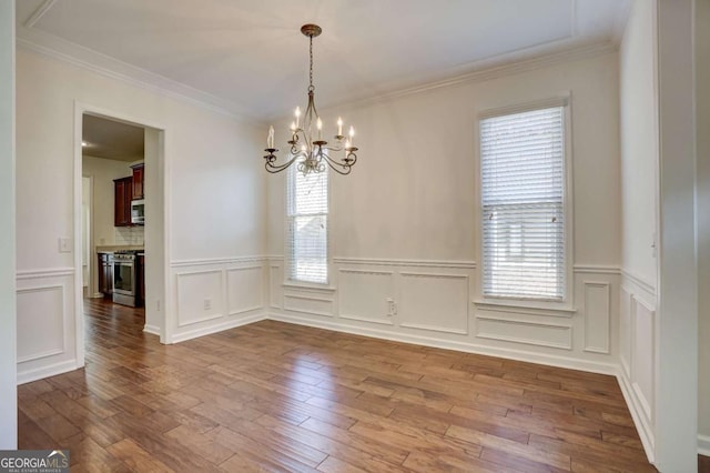 unfurnished dining area featuring wood-type flooring, crown molding, and a chandelier