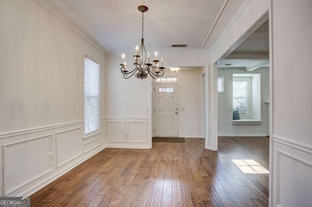 entryway with hardwood / wood-style flooring, crown molding, and an inviting chandelier