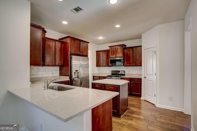 kitchen featuring sink, decorative backsplash, kitchen peninsula, stainless steel appliances, and light wood-type flooring