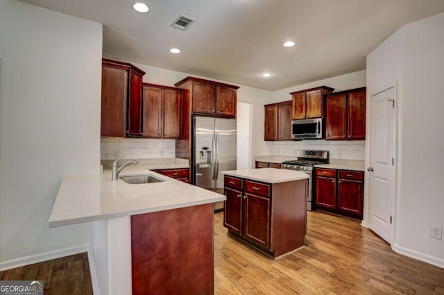 kitchen featuring tasteful backsplash, sink, light hardwood / wood-style floors, kitchen peninsula, and stainless steel appliances