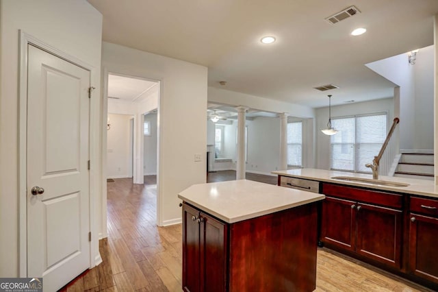 kitchen with pendant lighting, sink, light hardwood / wood-style flooring, decorative columns, and a kitchen island