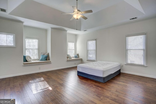 unfurnished bedroom featuring multiple windows, ceiling fan, dark hardwood / wood-style flooring, and a tray ceiling