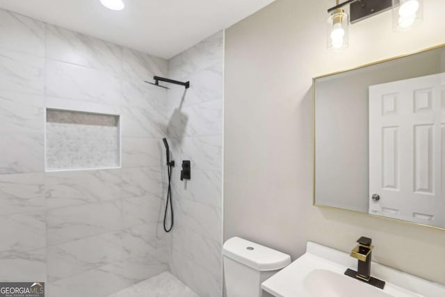 bathroom featuring vanity, a tile shower, and toilet