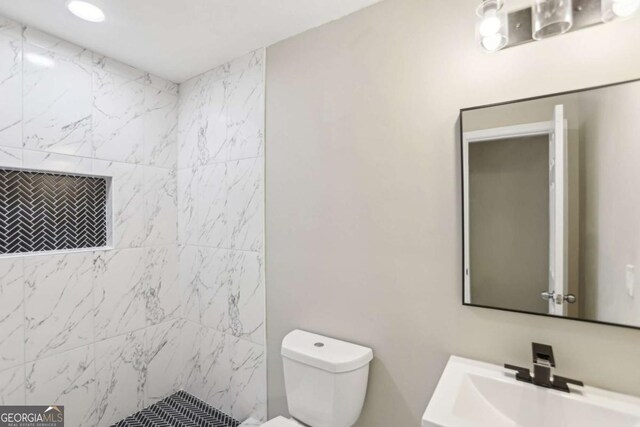 bathroom with tiled shower, vanity, and toilet