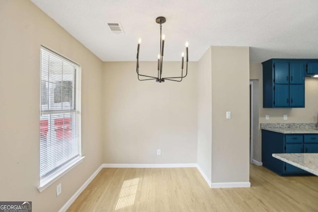 unfurnished dining area with an inviting chandelier and light wood-type flooring