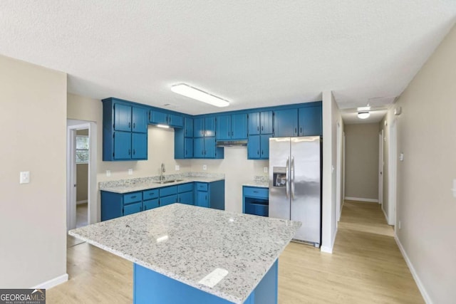 kitchen with a kitchen island, stainless steel refrigerator with ice dispenser, light stone countertops, blue cabinetry, and light hardwood / wood-style flooring