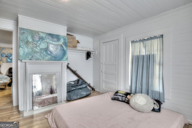 bedroom with crown molding, light hardwood / wood-style floors, and wood walls