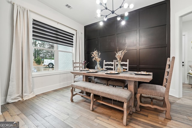 dining room featuring a decorative wall, a chandelier, light wood finished floors, baseboards, and visible vents