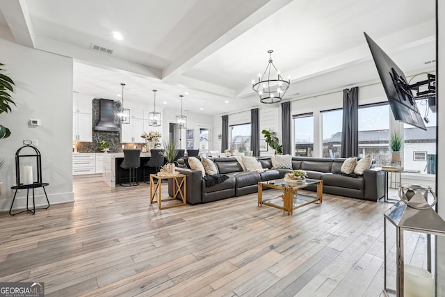 living room featuring beamed ceiling, a notable chandelier, visible vents, and light wood-style floors