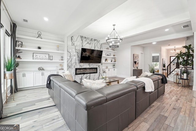 living room featuring stairs, a notable chandelier, light wood-style floors, and a fireplace