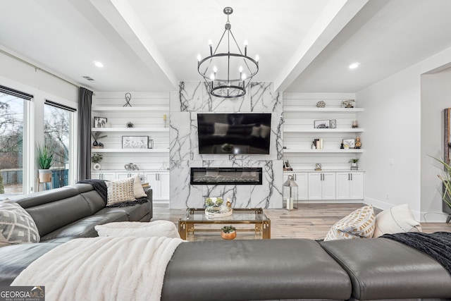living area featuring an inviting chandelier, light wood-type flooring, visible vents, baseboards, and a high end fireplace