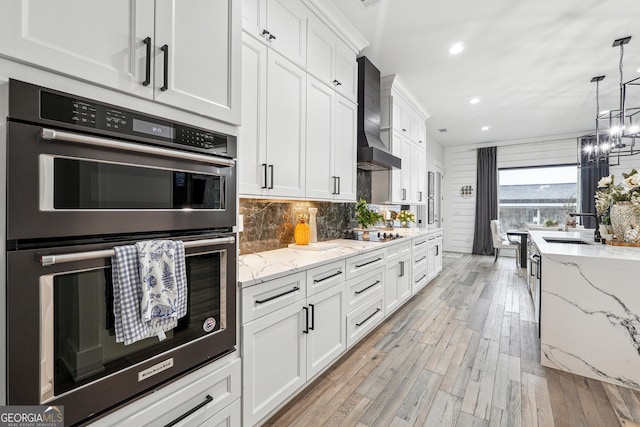 kitchen with double oven, tasteful backsplash, white cabinets, recessed lighting, and wall chimney exhaust hood