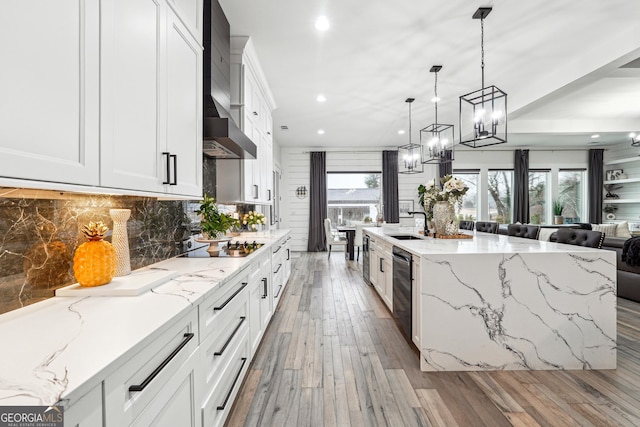 kitchen with light stone counters, an inviting chandelier, recessed lighting, wall chimney exhaust hood, and backsplash
