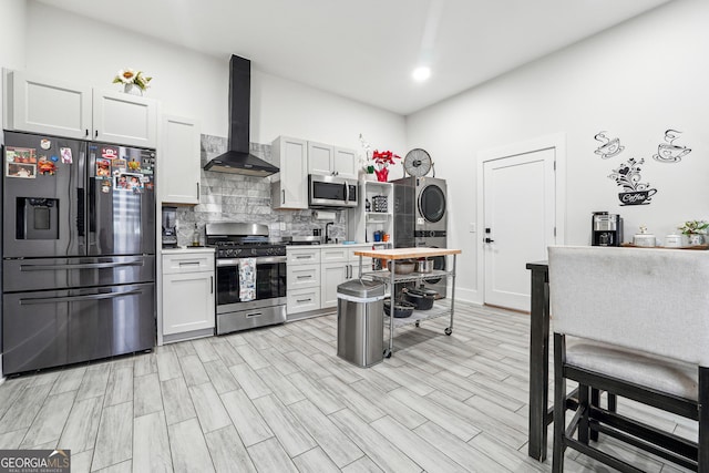 kitchen with stacked washer / drying machine, stainless steel appliances, light wood-style floors, tasteful backsplash, and wall chimney exhaust hood