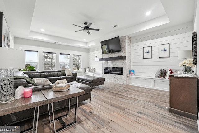 living room featuring visible vents, ceiling fan, hardwood / wood-style floors, a tray ceiling, and a high end fireplace