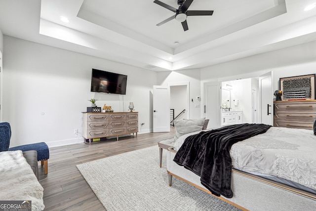 bedroom with wood finished floors, recessed lighting, a tray ceiling, and baseboards
