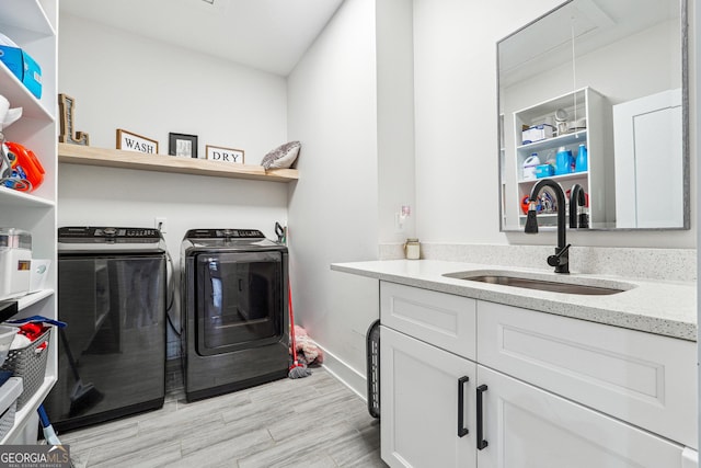 laundry room featuring attic access, a sink, washing machine and clothes dryer, cabinet space, and light wood-style floors