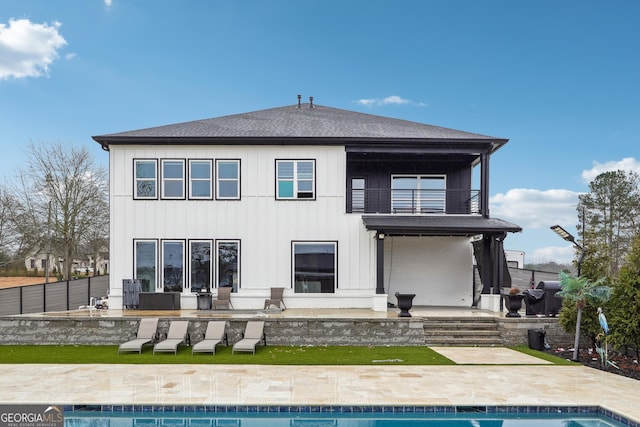 rear view of property featuring a patio, a shingled roof, a balcony, an outdoor pool, and fence