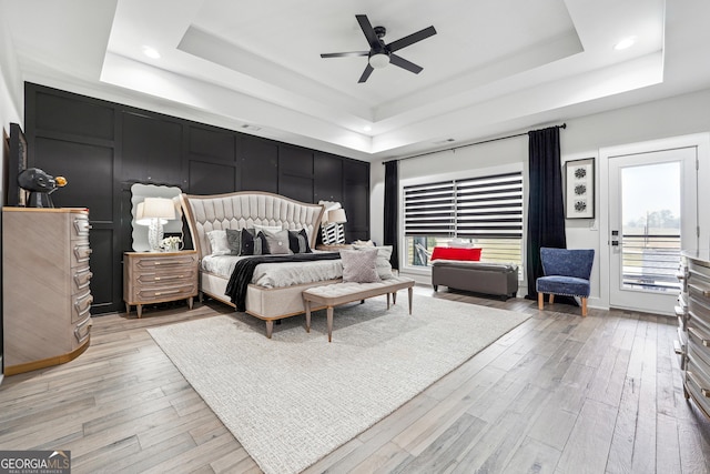 bedroom with recessed lighting, wood finished floors, access to exterior, and a tray ceiling