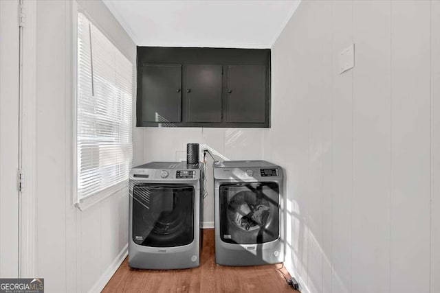 clothes washing area featuring hardwood / wood-style flooring, cabinets, and separate washer and dryer