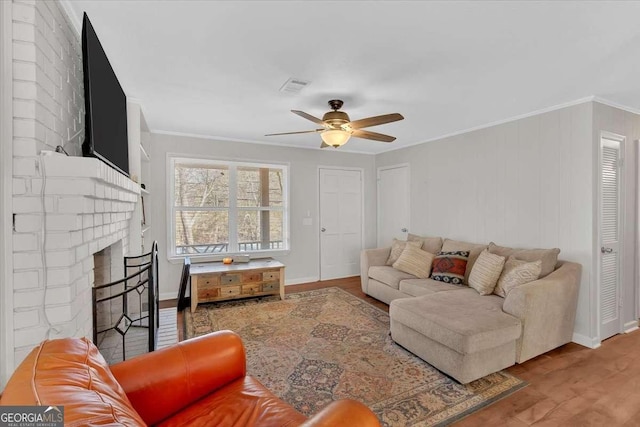 living room featuring crown molding, a brick fireplace, hardwood / wood-style floors, and ceiling fan