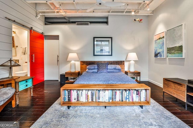 bedroom with a barn door, dark hardwood / wood-style floors, and track lighting