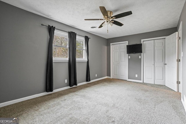 unfurnished bedroom featuring ceiling fan, carpet flooring, two closets, and a textured ceiling