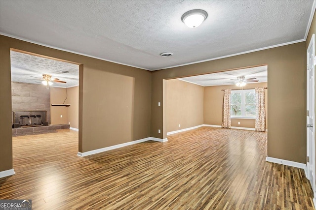 empty room featuring a fireplace, crown molding, wood-type flooring, and ceiling fan