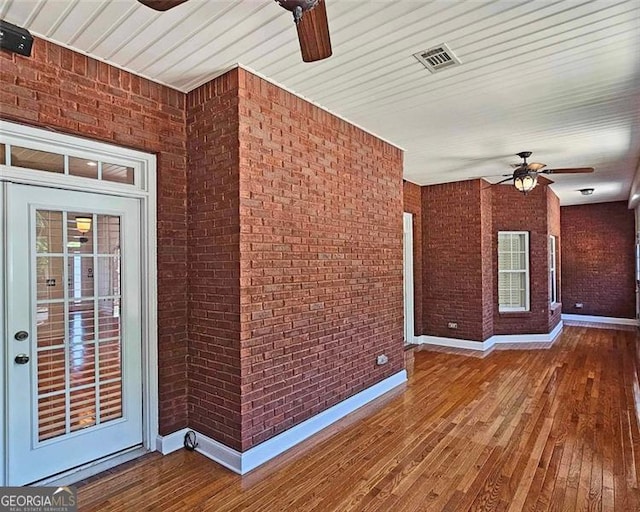 interior space with brick wall, hardwood / wood-style floors, and ceiling fan