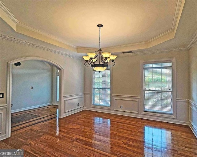 unfurnished dining area with crown molding, dark hardwood / wood-style floors, an inviting chandelier, and a tray ceiling