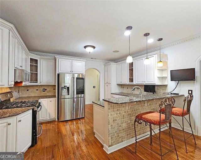 kitchen with pendant lighting, appliances with stainless steel finishes, white cabinets, a kitchen bar, and kitchen peninsula