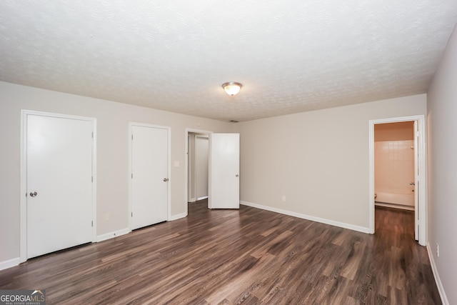 unfurnished bedroom with dark hardwood / wood-style floors, a textured ceiling, and ensuite bathroom